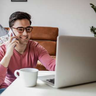 A young man with a laptop at home, he is working and writing notes in a notebook